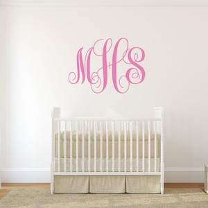 May include: Pink monogram decal with the letters MHS in a cursive font on a white wall above a white crib with a white mattress and a white rug on the floor.