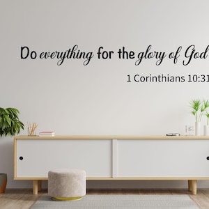 May include: White wall with a black cursive quote that reads "Do everything for the glory of God" with the scripture reference "1 Corinthians 10:31" below it. A white dresser with two drawers and a light brown top sits in front of the wall.