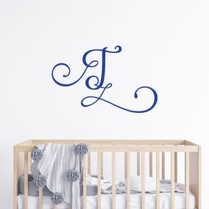 May include: A white cot with a blue and white blanket and a blue cursive letter "J" on the wall above it.