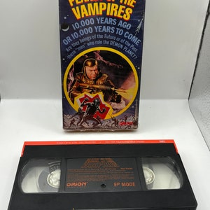 Puede incluir: Una caja de cinta VHS y una cinta para la película "Planeta de los Vampiros". La caja presenta una imagen en blanco y negro de un hombre con un traje espacial futurista sosteniendo un arma. El texto en la caja dice "Planeta de los Vampiros", "Hace 10.000 años o dentro de 10.000 años", y "¿Son seres del futuro o del pasado, estos "hombres" que gobiernan el PLANETA DEMONIO?"