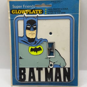 May include: A vintage Batman Glowplate light switch cover. The cover features a blue and black Batman graphic with a yellow bat symbol. The packaging reads "Super Friends" and "Glows in the Dark."