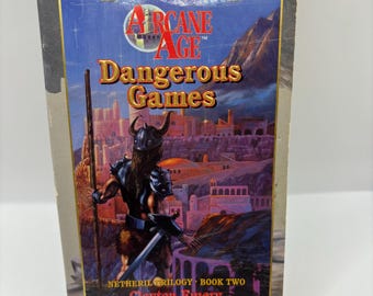 May include: A paperback book cover with a fantasy illustration of a warrior standing on a bridge overlooking a city. The book title is "Arcane Age Dangerous Games" and the subtitle is "Netheril Trilogy - Book Two" by Clayton Emery.
