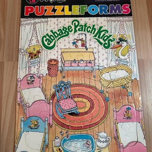 May include: A Colorforms Puzzleforms Cabbage Patch Kids 30-piece puzzle featuring a nursery scene with a changing table, rocking chair, cribs, and a bathtub. The packaging includes the text Colorforms, Puzzleforms, and Cabbage Patch Kids.