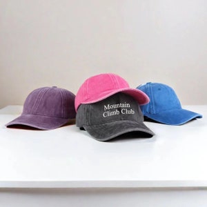 Könnte beinhalten: Drei Baseballkappen, eine rosa, eine lila und eine blaue, mit einer schwarzen Kappe, auf der der Text "Mountain Climb Club" vorne gestickt ist.