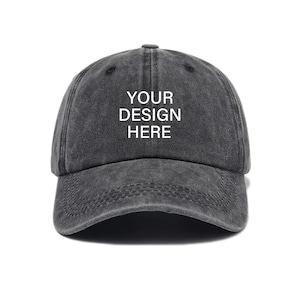 Pu&ograve; includere: Un cappello da baseball in cotone nero, usurato, con il testo "YOUR DESIGN HERE" in bianco.