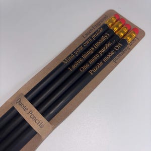May include: Four black pencils with red erasers, each laser-engraved with a different quote. The pencils are presented in a brown cardboard sleeve labelled "Quote Pencils".