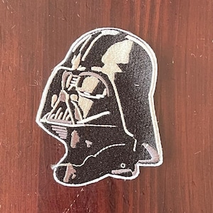 May include: Black and white embroidered patch of Darth Vader's helmet from Star Wars.