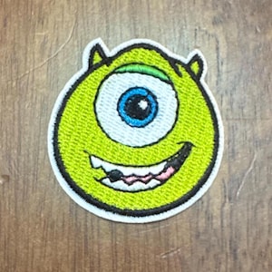May include: Green one-eyed monster character with a toothy grin, embroidered patch.