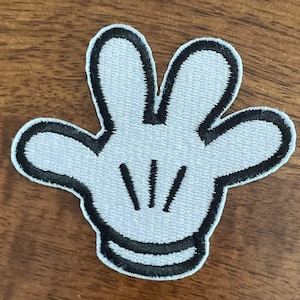 May include: White felt glove with black stitching, resembling a cartoon hand with four fingers. The glove has three black lines in the center, representing the palm lines.