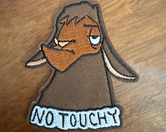 May include: Embroidered patch featuring a cartoon character with a grumpy expression. The character is brown and orange, with the words "NO TOUCHY" in white on a blue background.