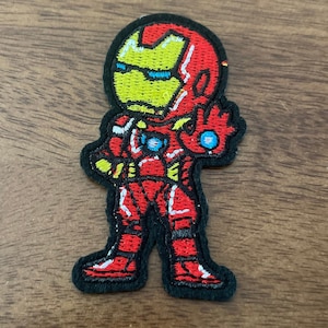May include: Iron Man embroidered patch with a red and yellow color scheme. The patch features a cartoon-style Iron Man with a black outline.