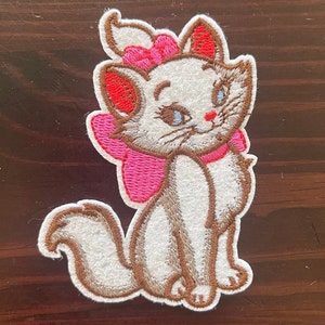 May include: White embroidered cat with pink bow and brown details. The cat is sitting with its tail curled behind it.