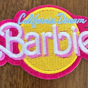 May include: A pink and white embroidered patch with the words "California Dream" and "Barbie" in a yellow circle.