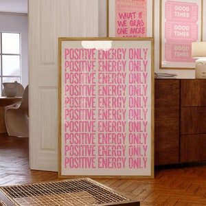 Może przedstawiać: R&oacute;żowo-biały plakat motywacyjny z tekstem "POSITIVE ENERGY ONLY" powt&oacute;rzonym 10 razy. Plakat jest oprawiony w jasną drewnianą ramę i wisi na ścianie.