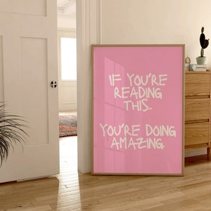 May include: A pink framed poster with white text that reads "If you're reading this... you're doing amazing."