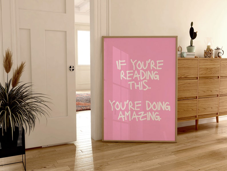 May include: A pink framed poster with white text that reads "If you're reading this... you're doing amazing."
