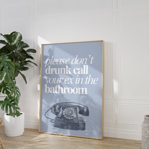 May include: A blue poster with a white frame and the text "please don't drunk call your ex in the bathroom" in white text. A black rotary phone is in the bottom center of the poster.
