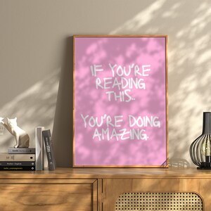 May include: Pink motivational poster with white text that reads "If you're reading this, you're doing amazing."