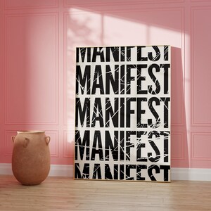 Pode incluir: Um p&ocirc;ster preto e branco com a palavra "MANIFEST" repetida cinco vezes em uma fonte desgastada. O p&ocirc;ster est&aacute; pendurado em uma parede rosa em uma sala com piso de madeira e um vaso de terracota.