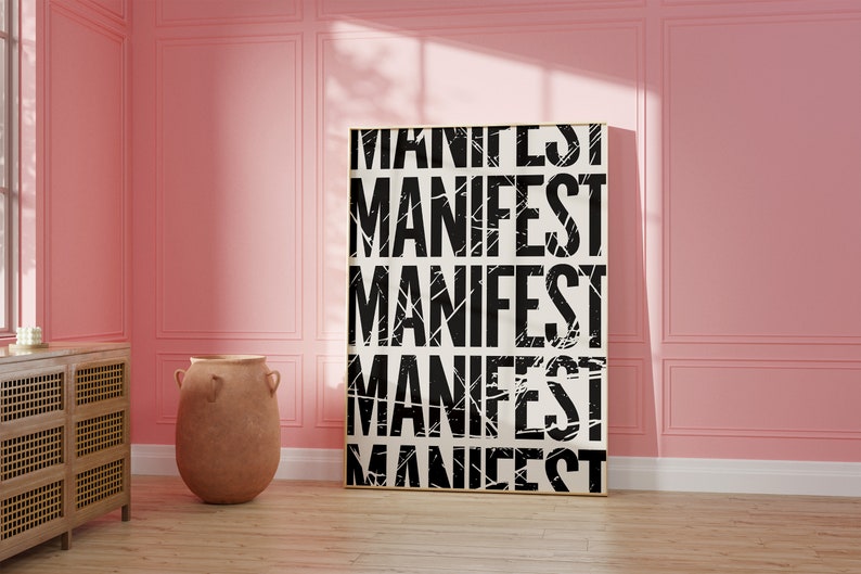 Pode incluir: Um p&ocirc;ster preto e branco com a palavra "MANIFEST" repetida cinco vezes em uma fonte desgastada. O p&ocirc;ster est&aacute; pendurado em uma parede rosa em uma sala com piso de madeira e um vaso de terracota.