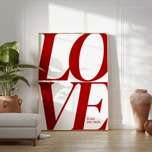 May include: A white poster with the word "LOVE" in large, red letters. The letters are stacked on top of each other. Below the word "LOVE" is the text "is all you need."