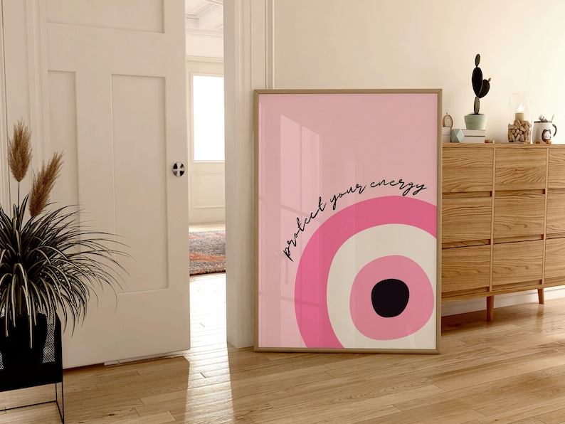 May include: A pink and white abstract print with a black circle in the center. The print is framed and has the text "protect your energy" written in black.