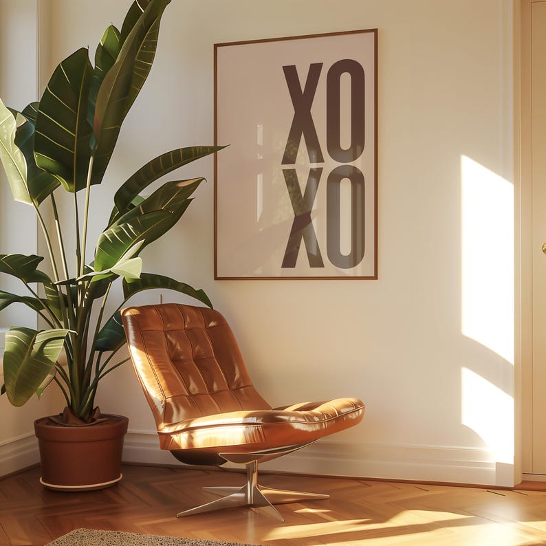 May include: A modern interior scene featuring a brown leather chair with a metal base, a large potted plant, and a framed print with the text "XO XO". The room has hardwood floors and is bathed in natural light.