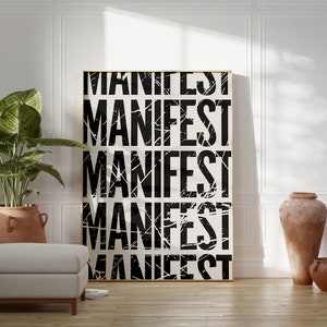 Pode incluir: Um p&ocirc;ster preto e branco com a palavra "MANIFEST" repetida cinco vezes em uma fonte desgastada. O p&ocirc;ster &eacute; emoldurado em uma moldura de madeira clara e est&aacute; pendurado em uma parede branca. Uma planta em vaso e dois vasos de terracota est&atilde;o em primeiro plano.