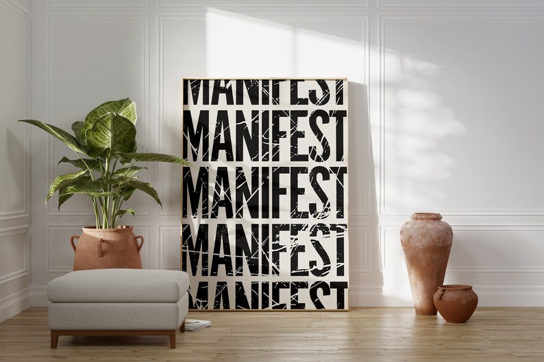 Pode incluir: Um p&ocirc;ster preto e branco com a palavra "MANIFEST" repetida cinco vezes em uma fonte desgastada. O p&ocirc;ster &eacute; emoldurado em uma moldura de madeira clara e est&aacute; pendurado em uma parede branca. Uma planta em vaso e dois vasos de terracota est&atilde;o em primeiro plano.