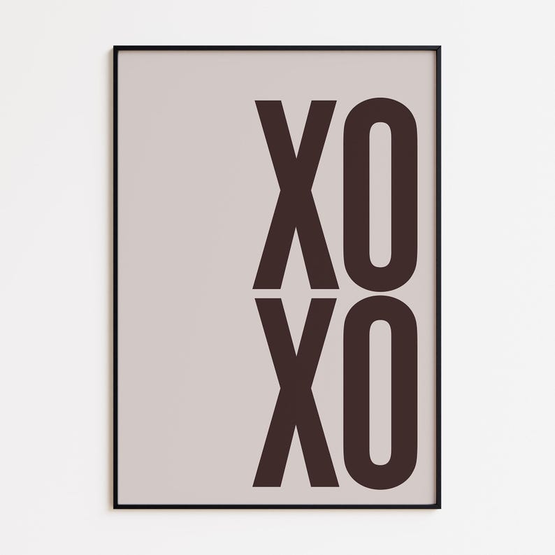 May include: A framed art print featuring the letters "XO" stacked vertically in a dark brown color. The background is a light beige, and the frame is black. The artwork is a simple, modern design.