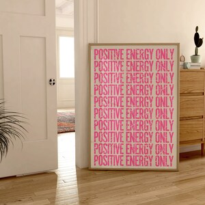 Może przedstawiać: Wydruk w ramie z tekstem "POSITIVE ENERGY ONLY" powt&oacute;rzonym r&oacute;żowymi literami na białym tle.