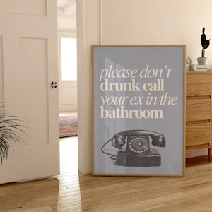 May include: A framed poster with a light blue background and white text that reads "please don't drunk call your ex in the bathroom". A black rotary phone is pictured in the bottom center of the poster.