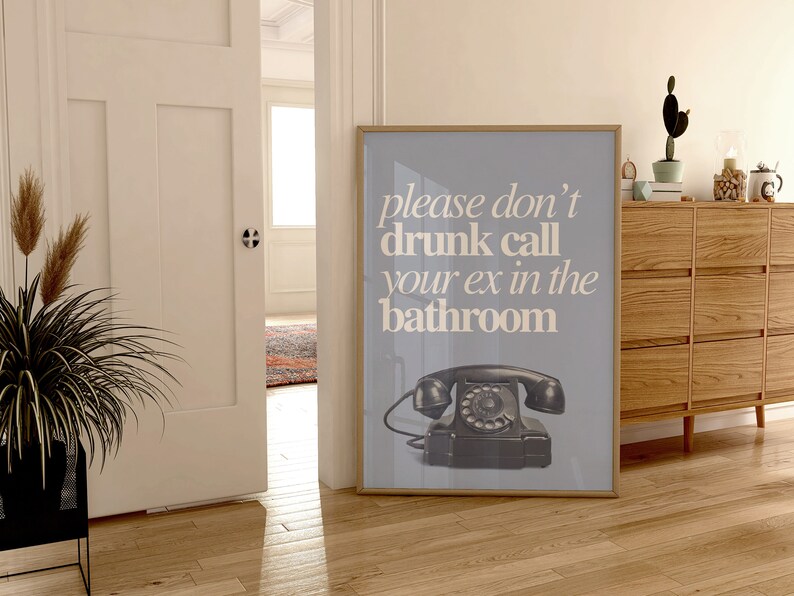May include: A framed poster with a light blue background and white text that reads "please don't drunk call your ex in the bathroom". A black rotary phone is pictured in the bottom center of the poster.