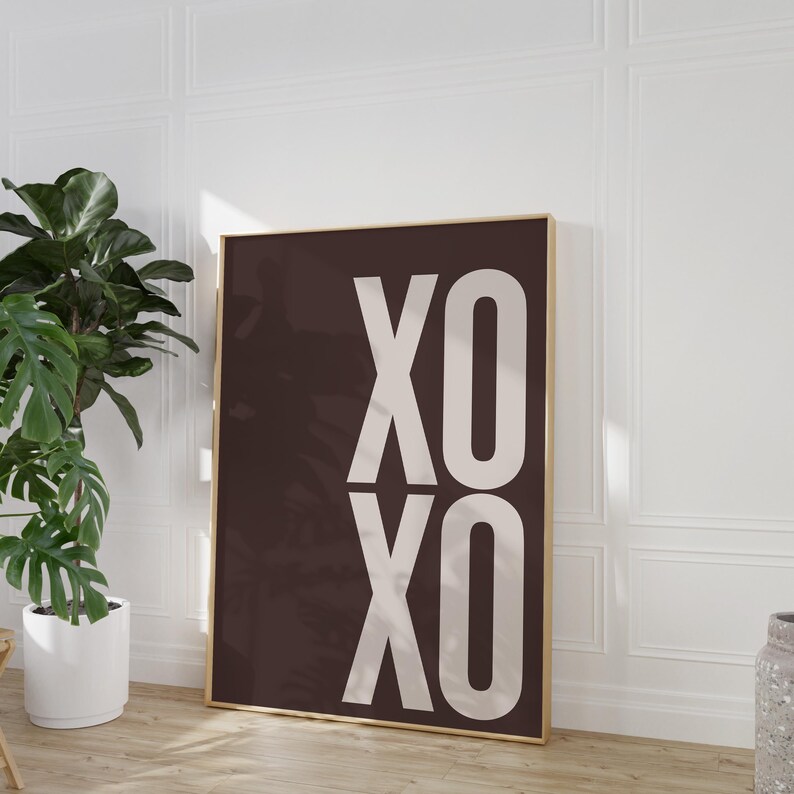 Może przedstawiać: Oprawiony wydruk z literami "XO" ułożonymi pionowo w powtarzalny wz&oacute;r. Litery są w jasnobeżowym kolorze na ciemnobrązowym tle. Rama jest złota.