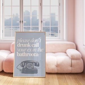 May include: A framed poster with a light blue background and white text that reads "please don't drunk call your ex in the bathroom". A black rotary phone is pictured below the text.