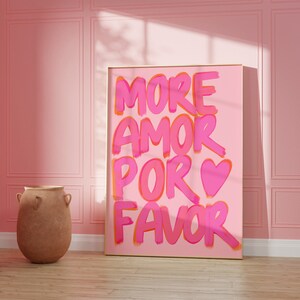 May include: A pink and orange framed canvas print with the text "MORE AMOR POR FAVOR" in a pink and orange handwritten font. A pink heart is included in the text.