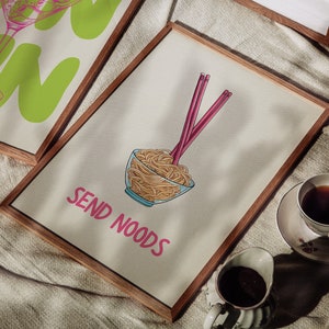 May include: Wooden framed art prints. One print features a green gin glass illustration with the word "GIN" in large letters. Another print shows a bowl of noodles with chopsticks and the text "SEND NOODS" in pink.