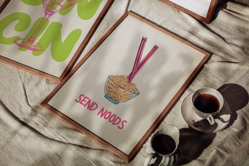 May include: Wooden framed art prints. One print features a green gin glass illustration with the word "GIN" in large letters. Another print shows a bowl of noodles with chopsticks and the text "SEND NOODS" in pink.