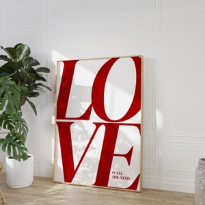 May include: A framed print with the word "LOVE" in large, bold, red letters on a white background. The text "IS ALL YOU NEED." is in smaller red letters at the bottom of the print.