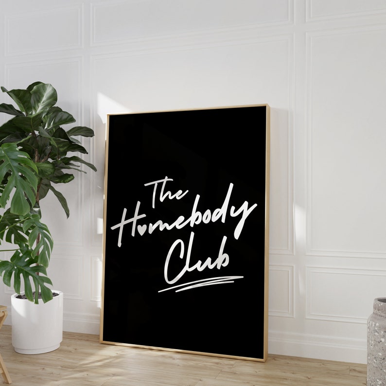 May include: Black and gold framed print with white text that reads "The Homebody Club" on a black background.