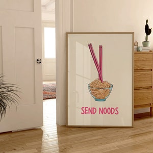 May include: A framed print featuring a bowl of noodles with pink chopsticks. The bowl is clear with a blue rim. The text "SEND NOODS" is below the bowl in pink. The print is displayed in a room with wooden floors.
