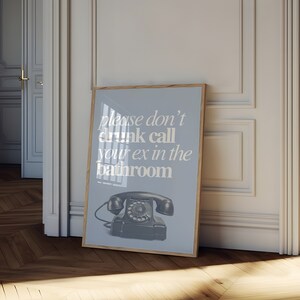 May include: A blue framed poster with a white background and the text "Please don't drunk call your ex in the bathroom". A vintage rotary phone is pictured below the text.