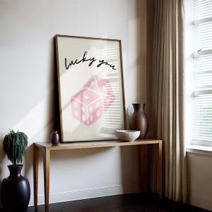 Pu&ograve; includere: Una stampa incorniciata con un design di dadi rosa e il testo "lucky you" in scrittura corsiva nera.