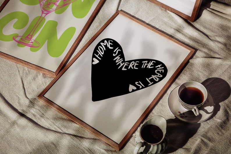 May include: A framed print with a black heart shape and the text "Home is where the heart is" in white. The print is on a white background and is framed in a natural wood frame.