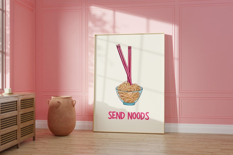 May include: A framed art print featuring a bowl of noodles with chopsticks. The image has a cartoon style with the words "SEND NOODS" in pink. The background is a light beige color.