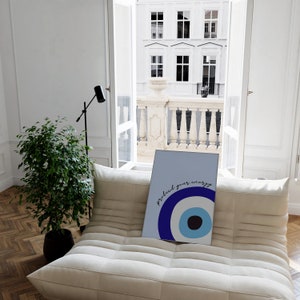 May include: A blue and white evil eye print with the text "protect your energy" on a light blue background. The print is on a white couch in a room with a window and a plant.