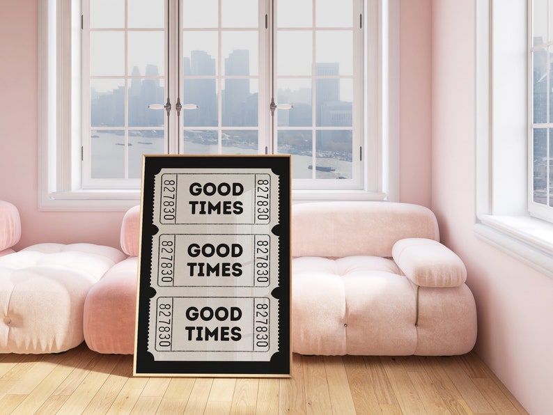 May include: A black framed print with three white tickets that say "Good Times" on a pink couch in a room with windows.