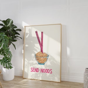 May include: A framed art print featuring a bowl of noodles with pink chopsticks. The words "SEND NOODS" are written in pink below the bowl. The artwork is set against a cream background.