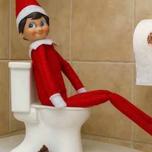 May include: A small elf doll with dark hair and blue eyes wearing a red suit with a white collar and a matching red hat. The doll is seated on a miniature white ceramic toilet with a pile of small brown chocolate chips placed on the base.