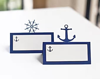 Puede incluir: Dos porta tarjetas de lugar azules y blancos con temas náuticos. Uno presenta una rueda de barco y el otro un ancla.